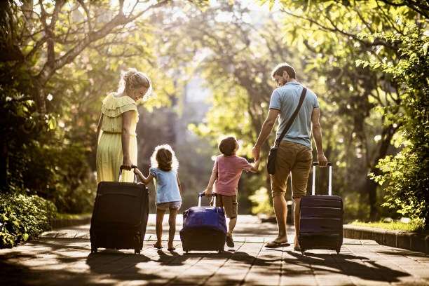 Rear view of parents and their kids pulling luggage in nature. Copy space.