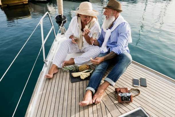 Senior couple drinking champagne on sailboat during summer vacation - Focus on man hand holding pineapple fruit